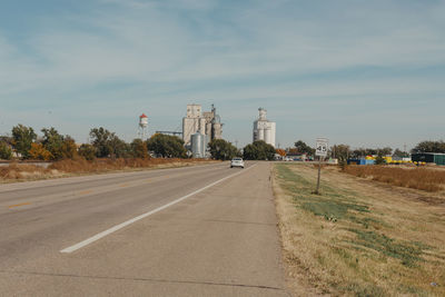 Road by farm town against sky