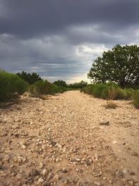 Dirt road on field against cloudy sky