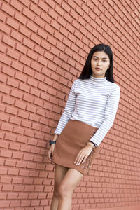 Portrait of young woman standing by brick wall