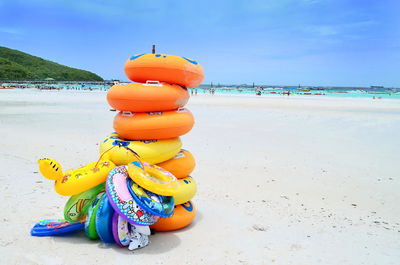 Stacked colorful inflatable rings at sandy beach against sky