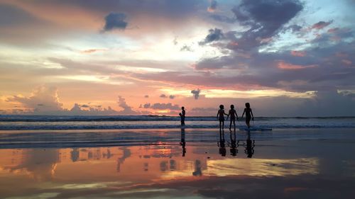Silhouette children at beach against cloudy sky during sunset