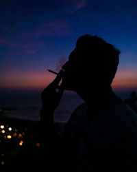 Silhouette man smoking cigarette against sky during a moody sunset. 