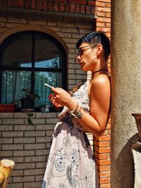 Young woman using mobile phone while standing by column