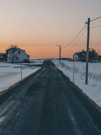 Road by snow covered landscape against sky during sunset