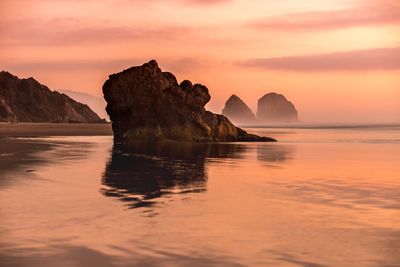 Rock formation in sea against sky during sunset