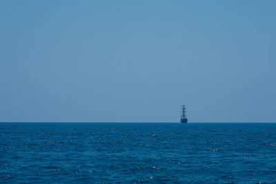 Lighthouse by sea against clear blue sky