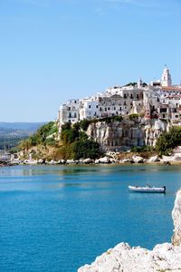 Buildings on cliff by sea against clear sky