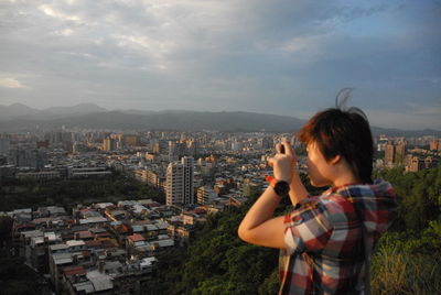 Young woman photographing against cityscape during sunset