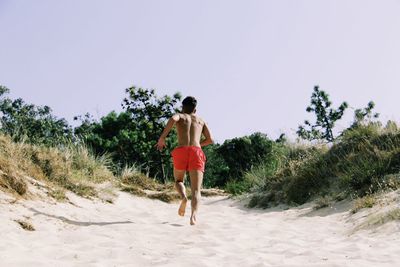 Rear view of man running on sand against clear sky