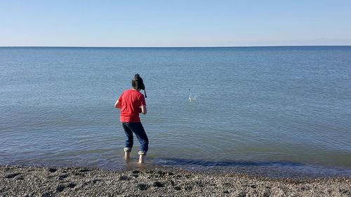 Rear view of woman standing on beach against clear sky