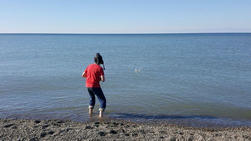 Rear view of man standing on beach against sky