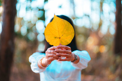 Midsection of woman holding yellow leaf during autumn