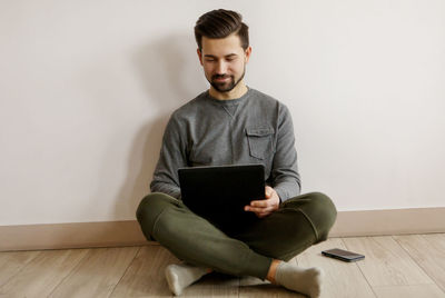 Young man using mobile phone while sitting on hardwood floor