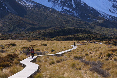 Friends walking on boardwalk amidst plants against mountains