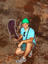 Full length portrait of smiling man crouching by rock formations at night