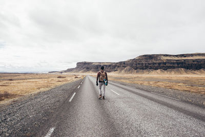 Rear view of man holding skateboard walking on road against mountain