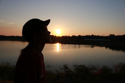 Silhouette young woman by lake against sky during sunset