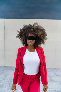 Curly hair woman with blindfold standing against wall