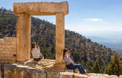 Women sitting on old ruin against mountains