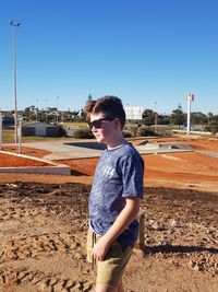 Boy standing on field against clear blue sky