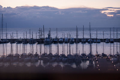 Sailboats moored in harbor at sunset