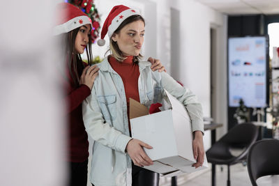 Portrait of smiling young woman using mobile phone while standing in office