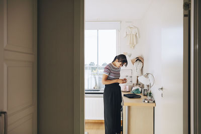 Teenage girl using mobile phone while standing by cabinet in bedroom at home