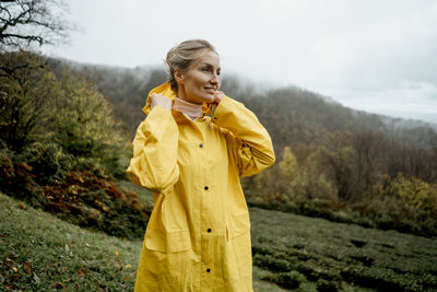 Pretty woman in yellow raincoat walking in rainy weather in the countryside
