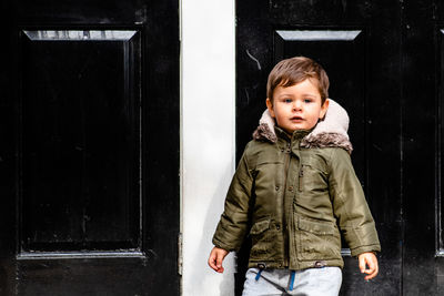 Portrait of cute boy standing against closed house door