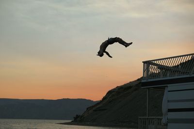 Full length of carefree man jumping into sea against sky during sunset