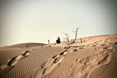 Man on sand dune in desert against clear sky