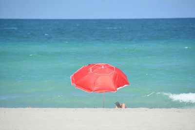 Red umbrella on beach against clear blue sky