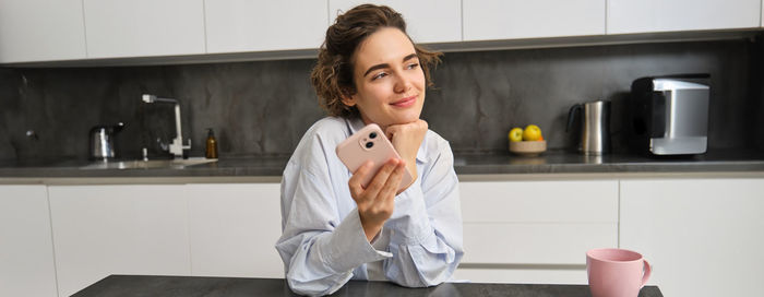 Portrait of young woman using mobile phone while sitting at home