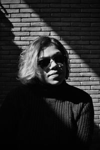 Portrait of young woman wearing sunglasses against brick wall