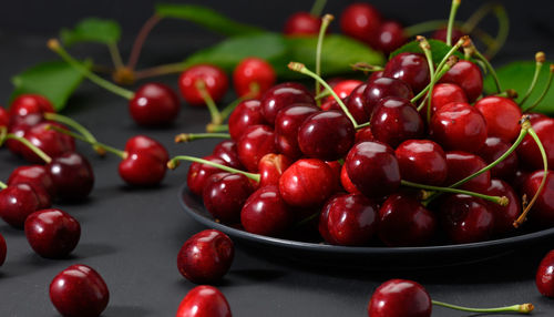 Ripe red cherries in a ceramic plate on a black wooden table