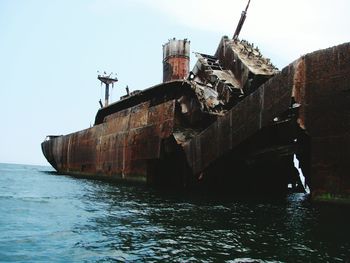 Metallic shipwreck in sea against clear sky