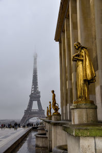 Low angle view of golden statue against an overcast sky and fog. eiffel tower in the background.