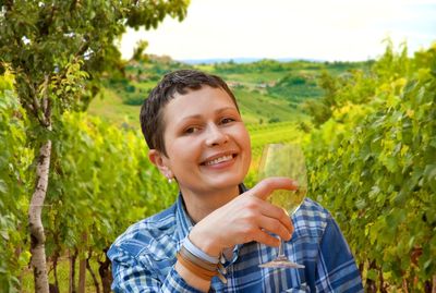 Portrait of smiling beautiful woman holding wineglass at vineyard