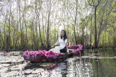 Portrait of woman sitting on pink flowering plants against trees