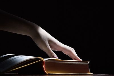 Person touching book against black background