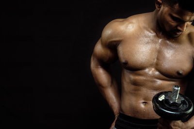Young man holding dumbbell against black background