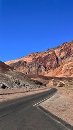 Road by mountain against clear blue sky