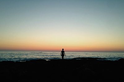 Silhouette person standing on beach against clear sky during sunset