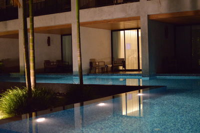 Empty chairs and table in swimming pool at night