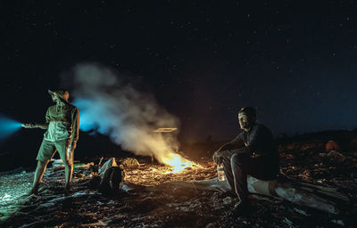 People sitting on bonfire against sky at night