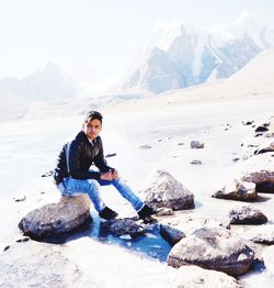 Portrait of man sitting on rock in river against mountains