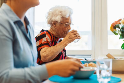 Senior woman drinking water while sitting with daughter at dining table