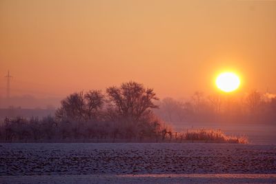 Scenic view of snow covered landscape against orange sky