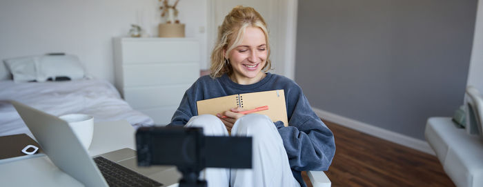 Portrait of young woman using digital tablet while sitting on bed at home