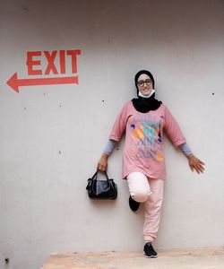 Full length portrait of young woman standing against wall